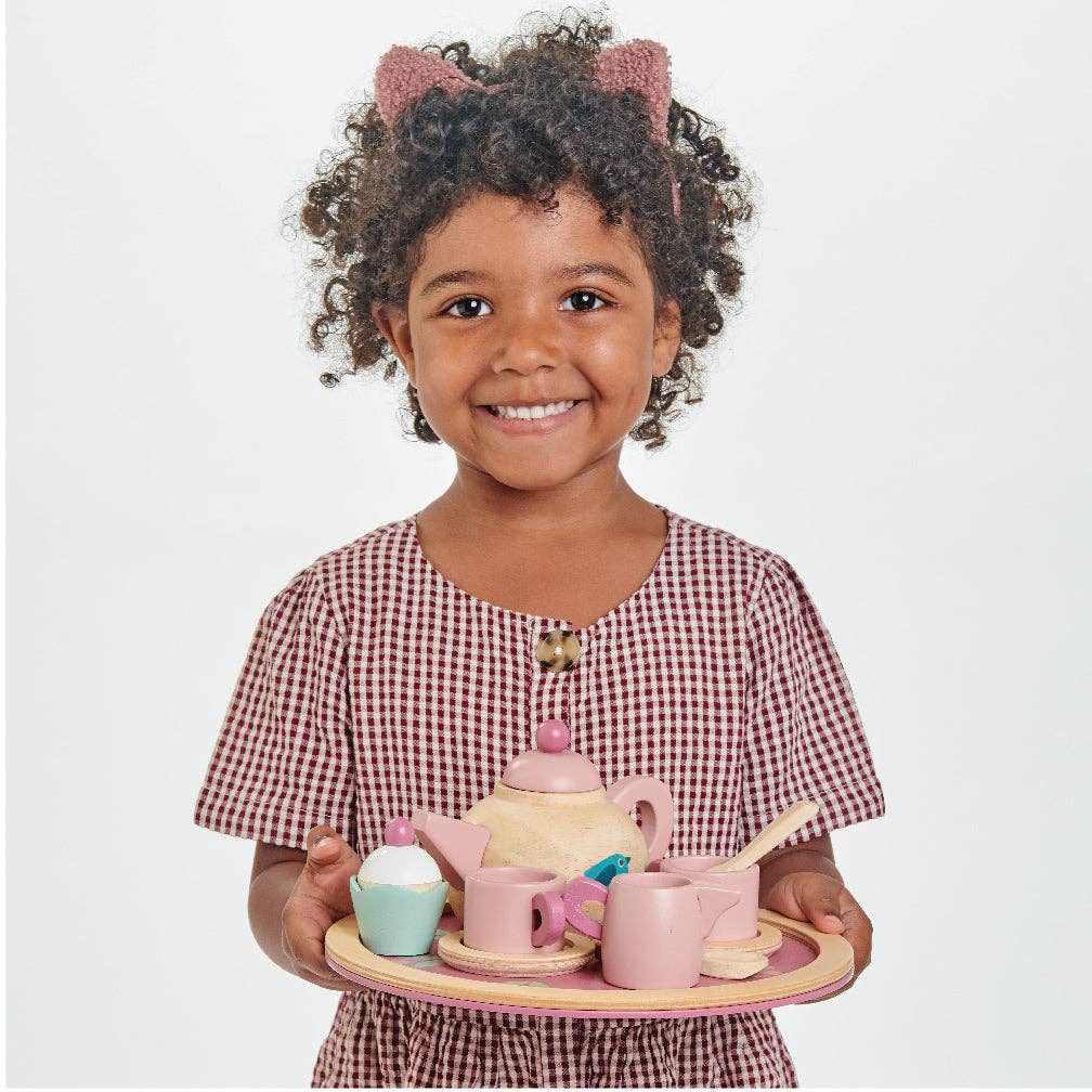 Smiling child holding the Birdie Tea Tray Set - Wooden Role Play Toy, a charming wooden tea set designed for pretend play with a delicate bird motif.