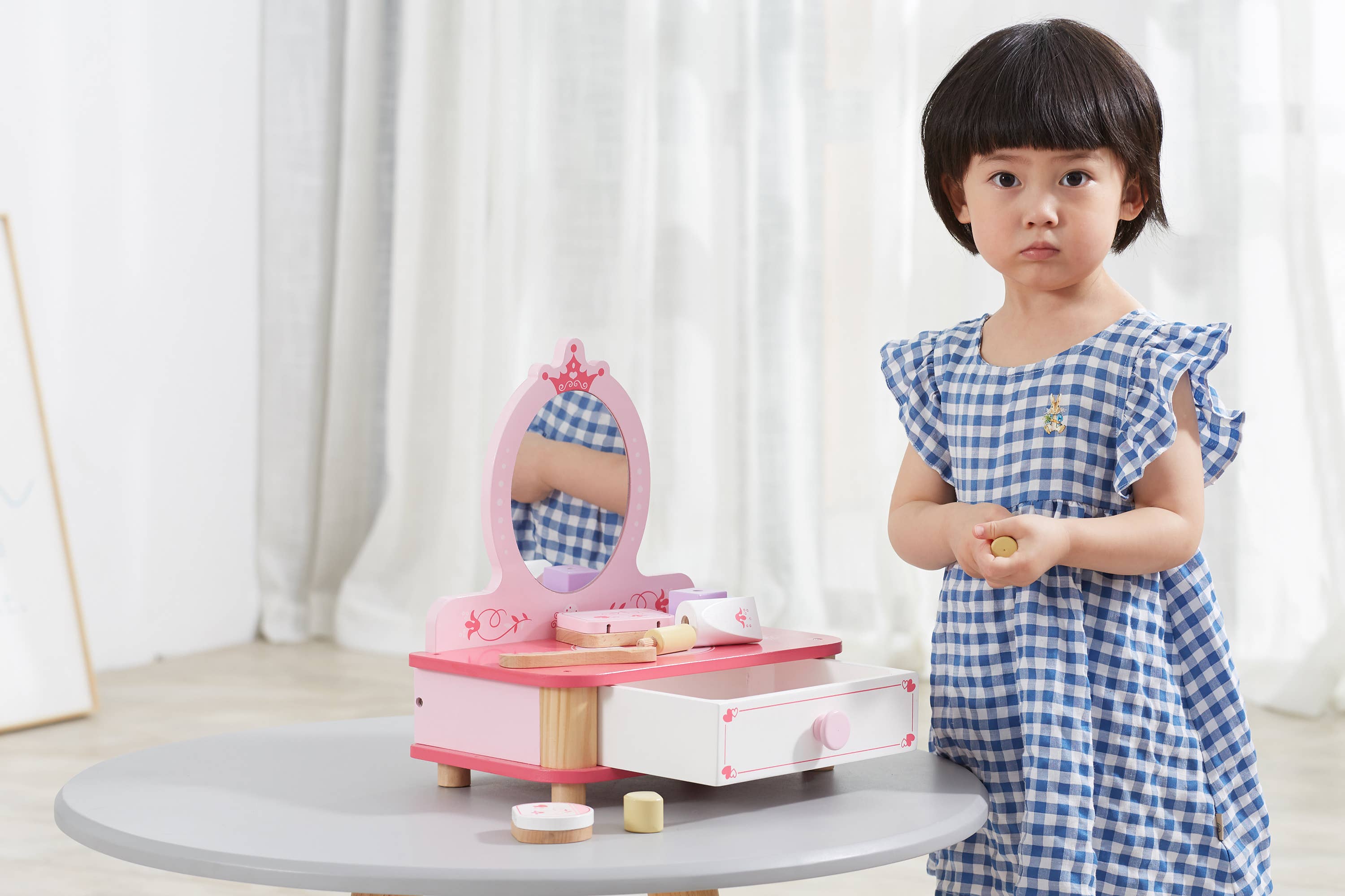 Young child playing with a wooden toy makeup set on a table. Encourages role play and creativity with a charming vanity design.