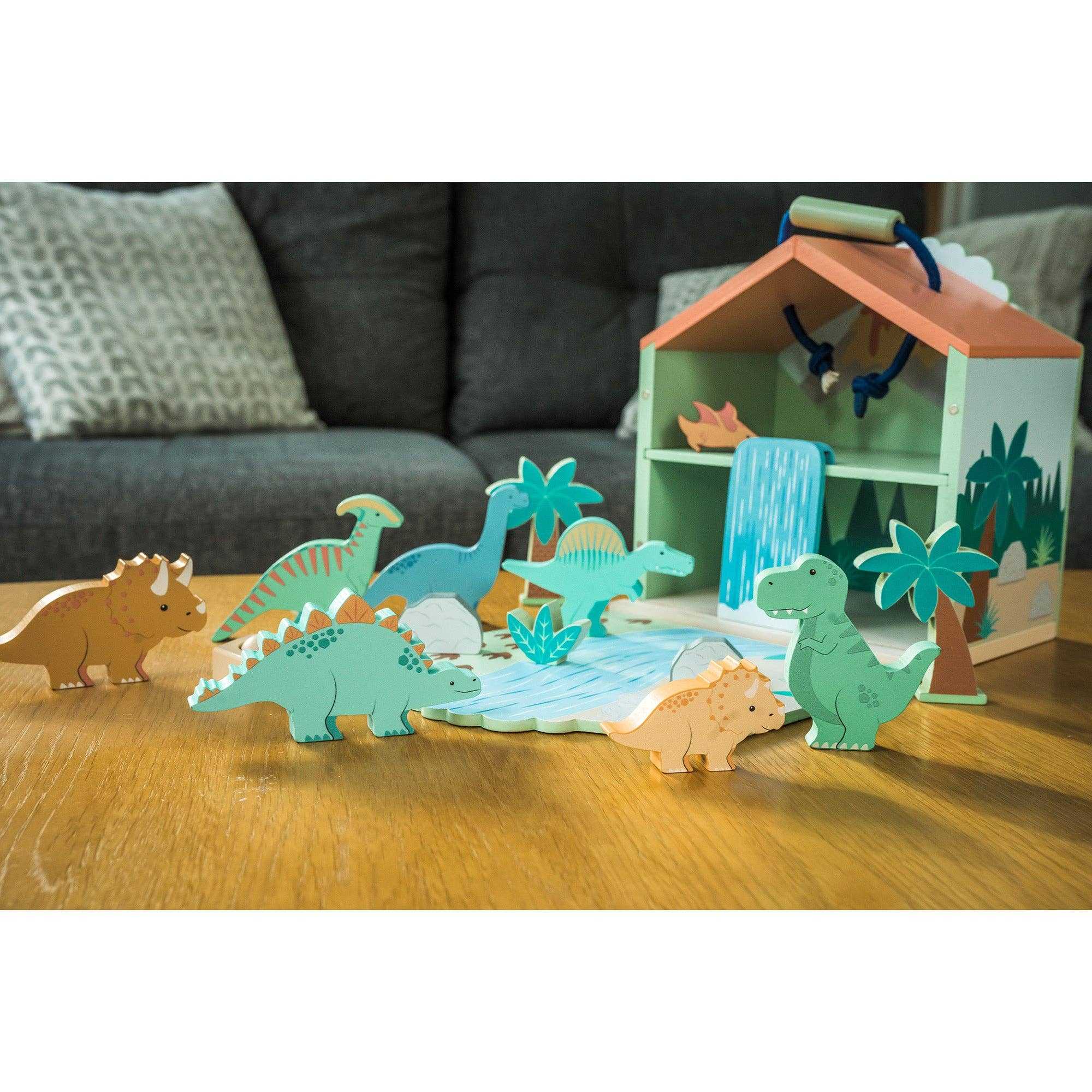 Wooden Dinosaur Toy Play Set by Orange Tree Toys displayed on a table with multiple dinosaur figures and scenic playhouse.