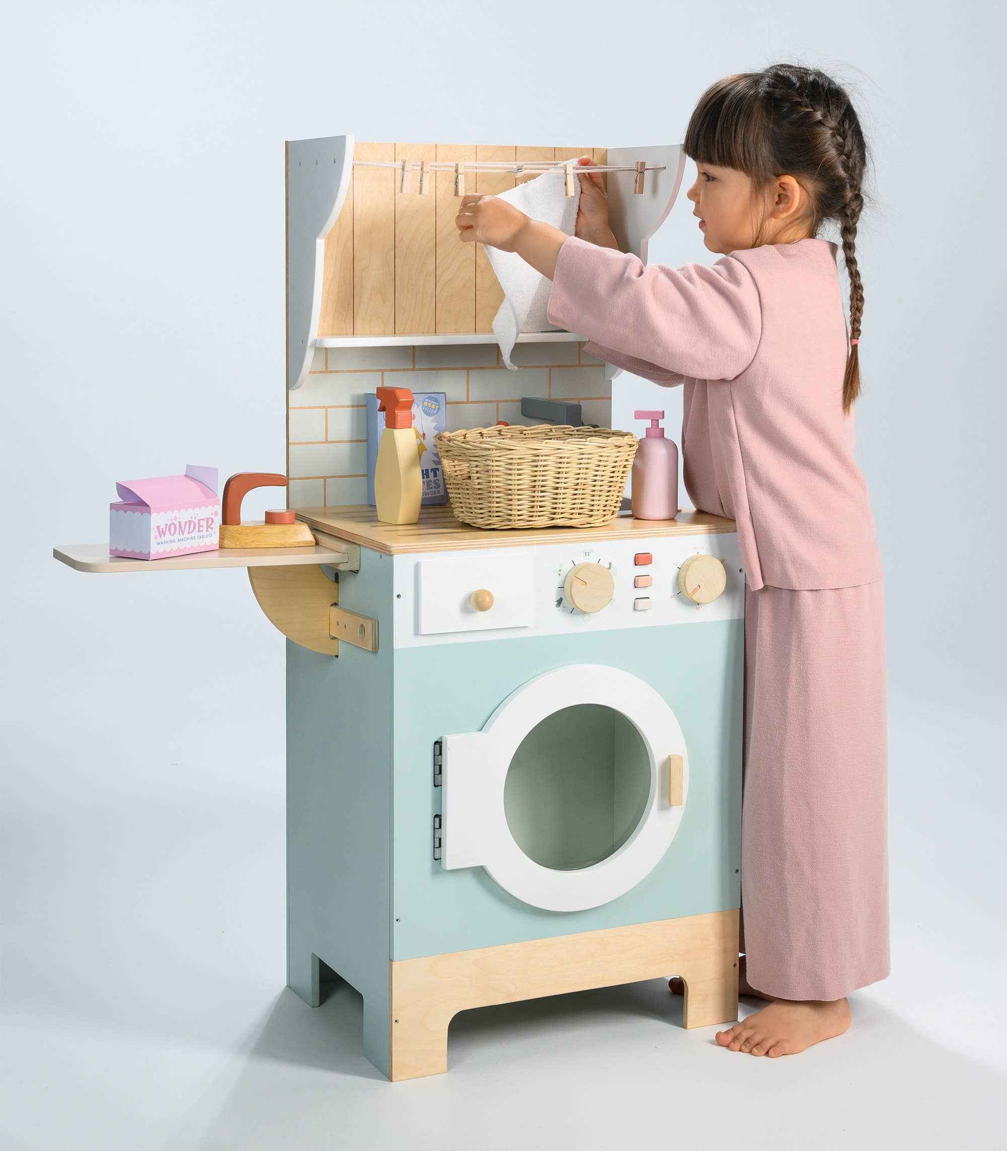 Child hanging towel on drying line of Tender Leaf Wooden Laundrette, engaging in imaginative housekeeping role play.