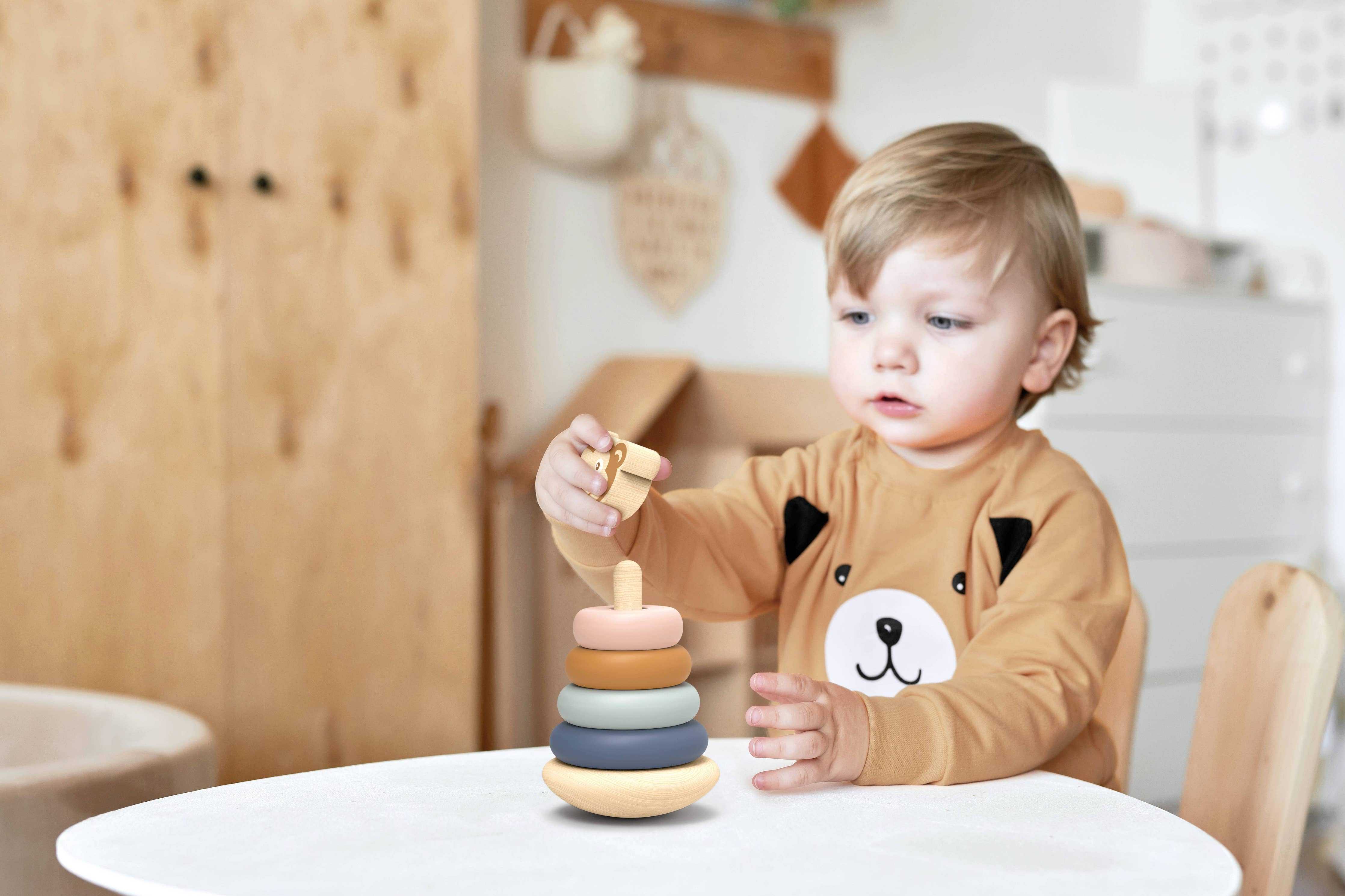 Toddler playing with Speedy Monkey Wooden Toy ring stacker on a table, a learning toy for age 12+ months promoting hand-eye coordination.