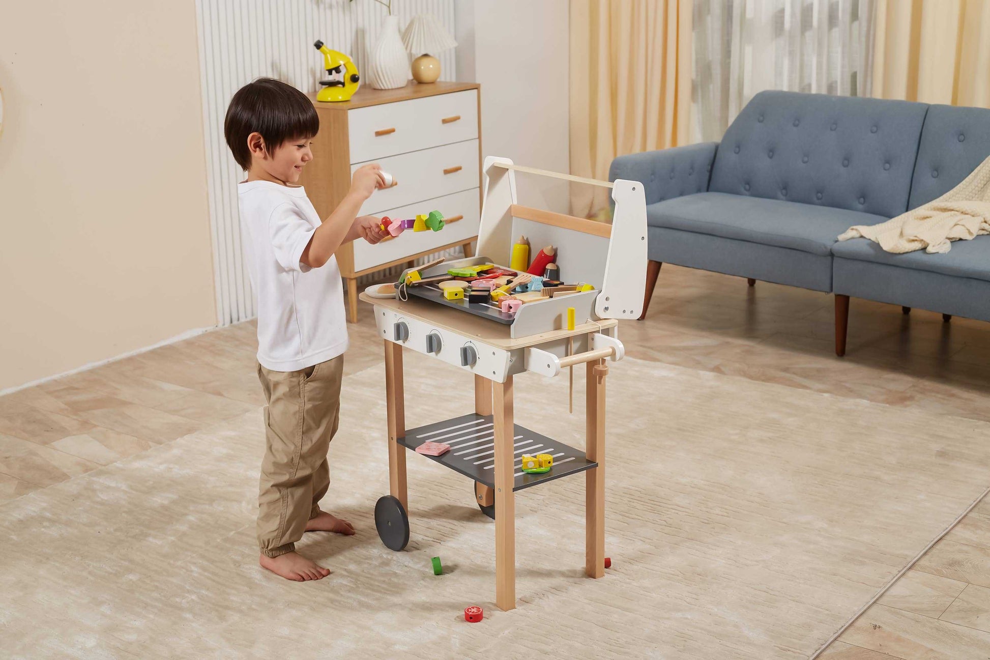 Child engaging with a wooden BBQ play set in a cozy living room, enhancing role-playing and social interaction skills.