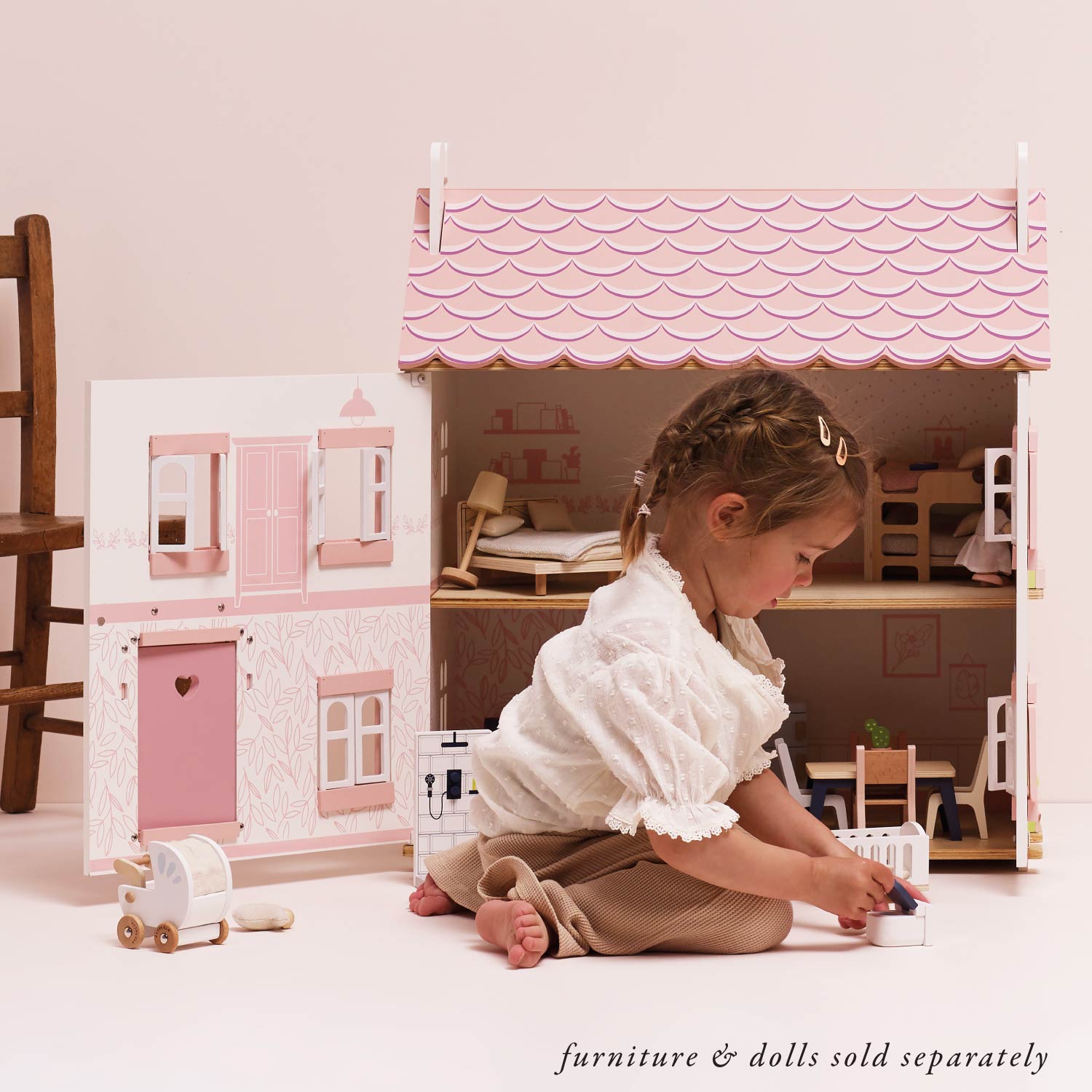Young girl playing with Le Toy Van Sophie's Wooden Dolls House interior, showcasing open rooms and wooden furniture setup.