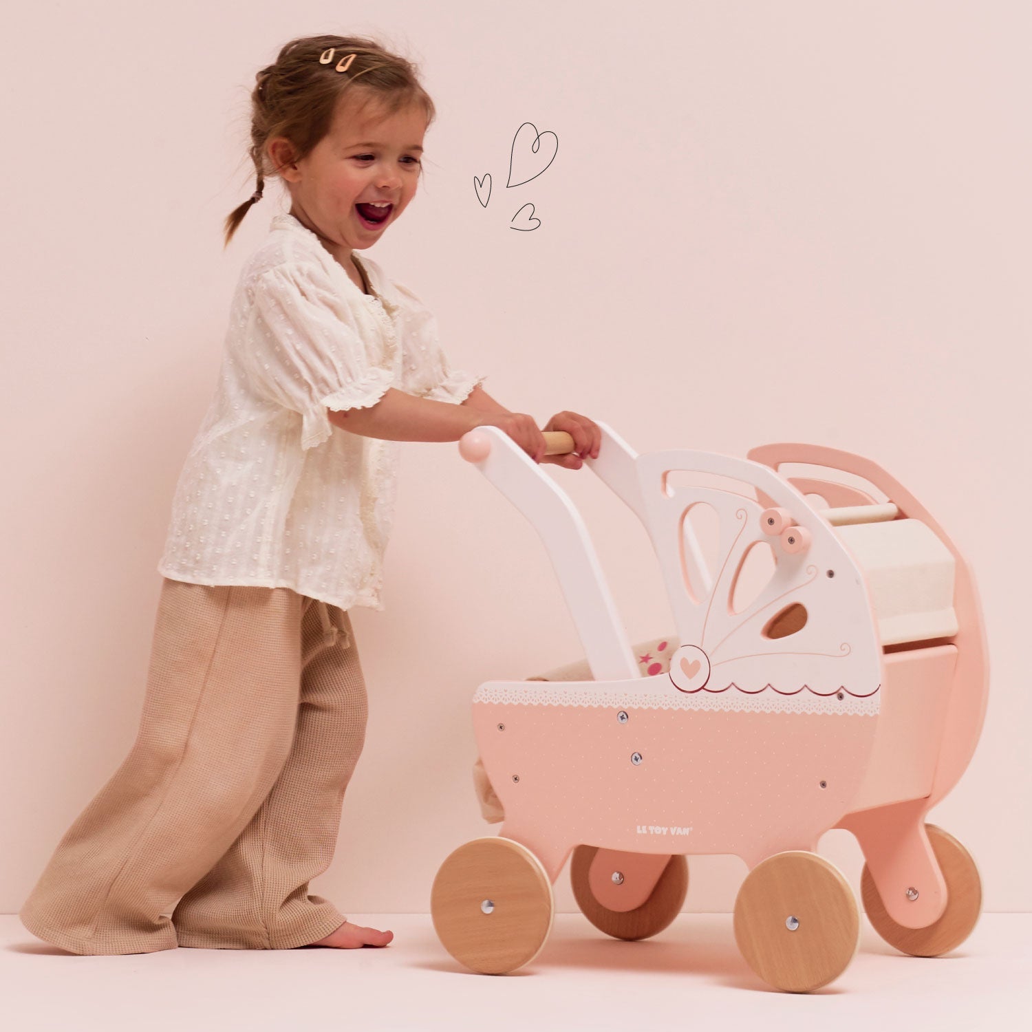 Young child playing with Ley Toy Van Retro Wooden Doll's Pram, demonstrating its roleplay function and easy-to-push design for toddlers aged 3+.
