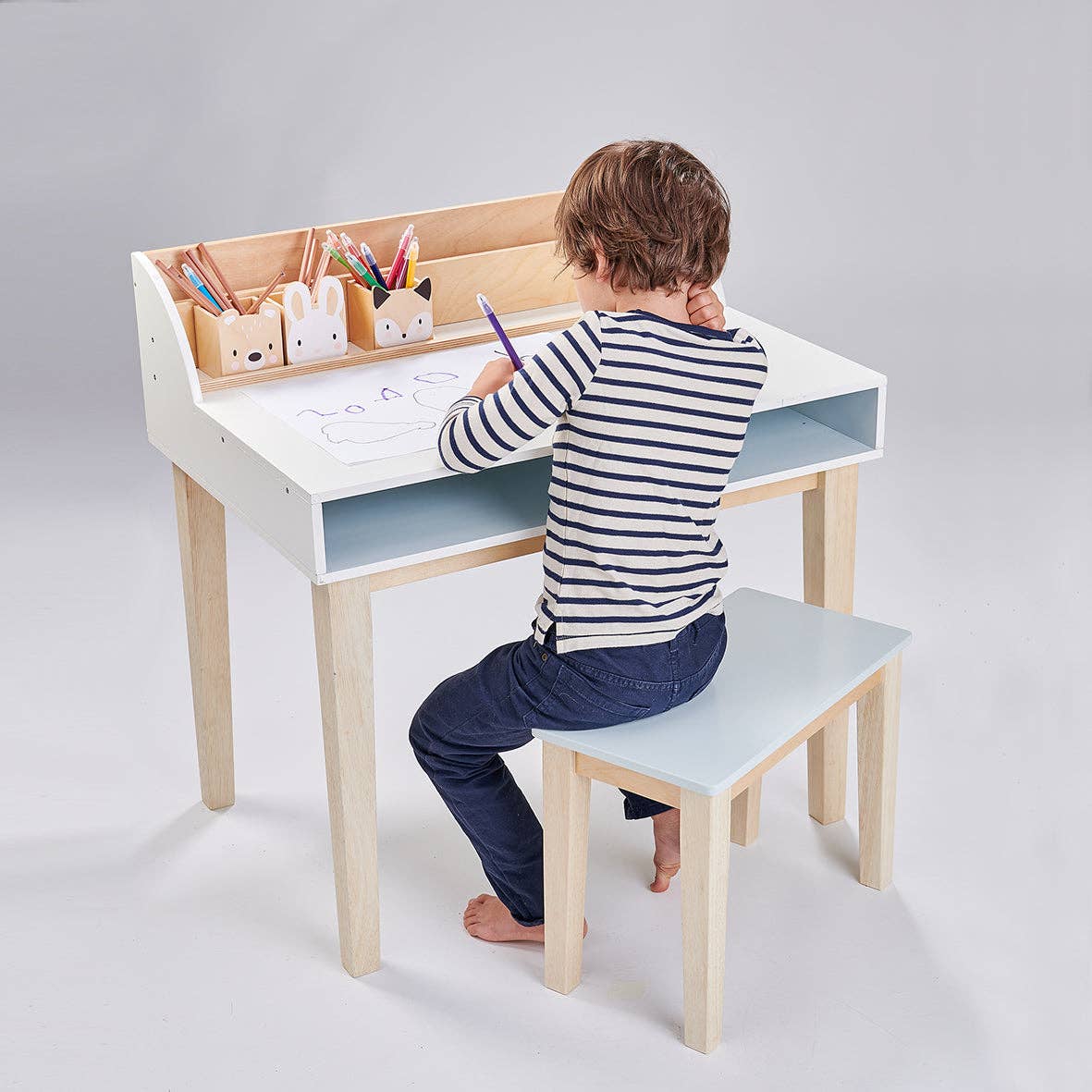 Young child drawing at the Childs Wooden Drawing Desk and Stool, featuring storage compartments and woodland animal-themed pen holders.