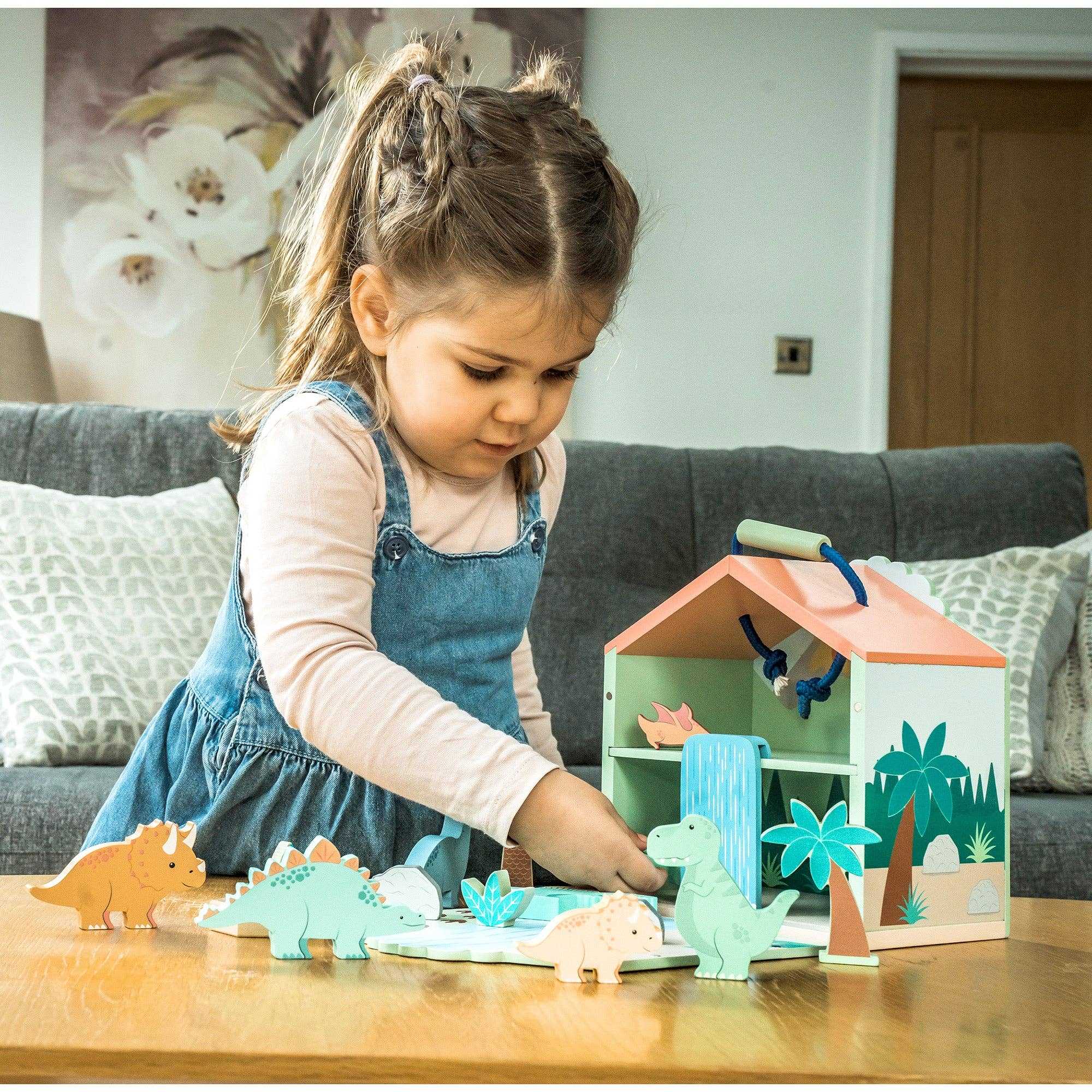 Child playing with Wooden Dinosaur Toy Play Set by Orange Tree Toys, engaging with colorful dinosaur figures and fold-out playhouse.