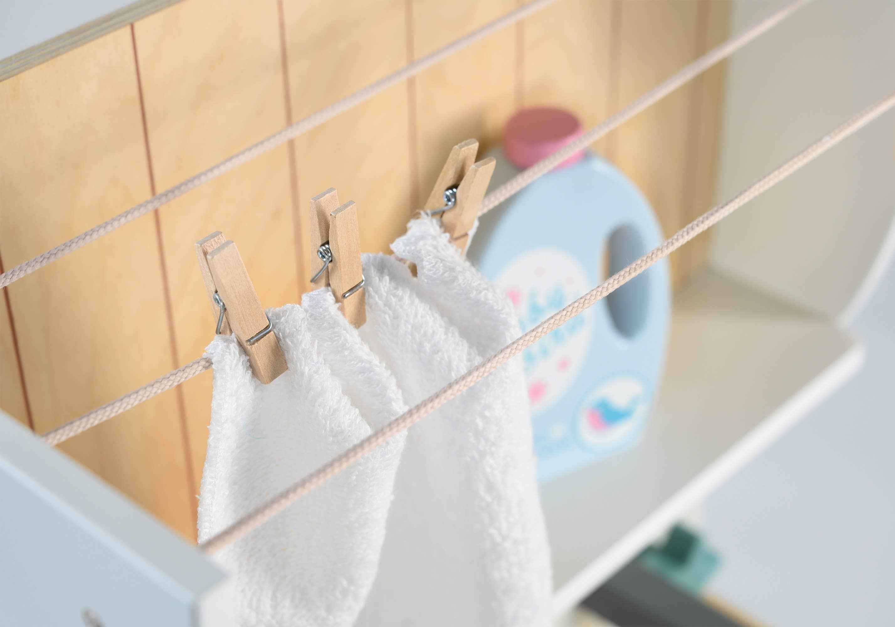 Close-up of Tender Leaf Wooden Laundrette's drying line with clothespins holding a towel and pretend detergent bottle on shelf.