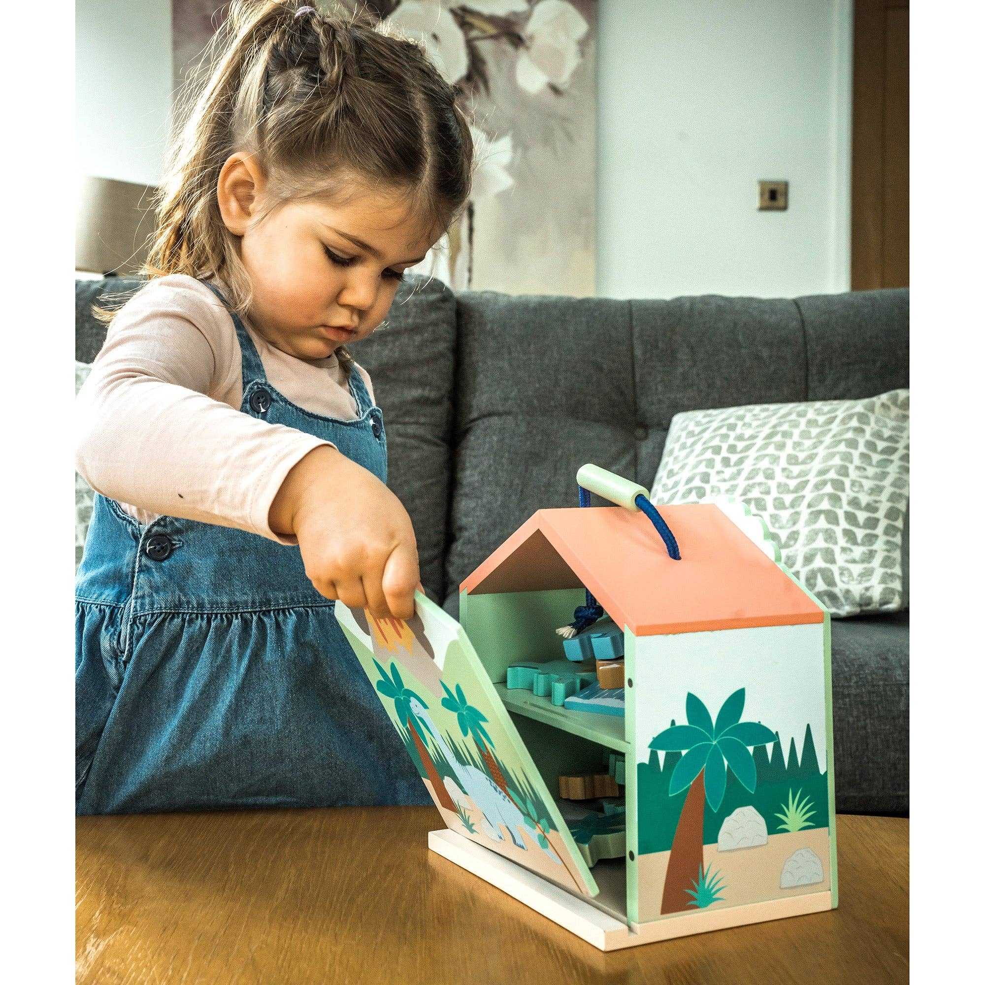 Child opening the fold-out playhouse from the Wooden Dinosaur Toy Play Set - 21 Pieces inc Trex by Orange Tree Toys.