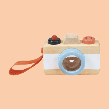 Wooden toy camera with a blue lens, orange wrist strap, and red and black buttons on top, set against a peach background.