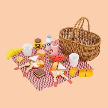 Toy picnic set with a wicker basket, red checkered mat, wooden play food including sandwiches, fruit slices, drinks, utensils, and cups arranged for pretend play.