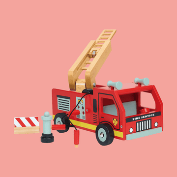 Wooden toy fire truck with an extendable ladder, fire hydrant, hose, and striped roadblock on a pink background.