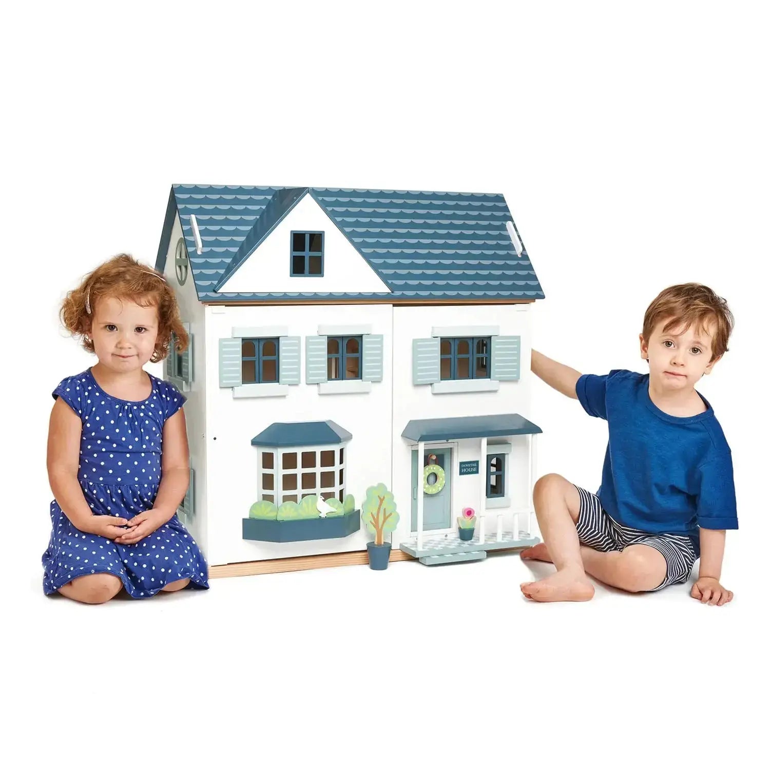 Two young children sitting beside the Dovetail House Wooden Dolls House, highlighting its large size and suitability for interactive play.